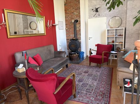Gemütlicher Raum mit Sofa, Sessel, einem alten Ofen vor eine roten Wand.