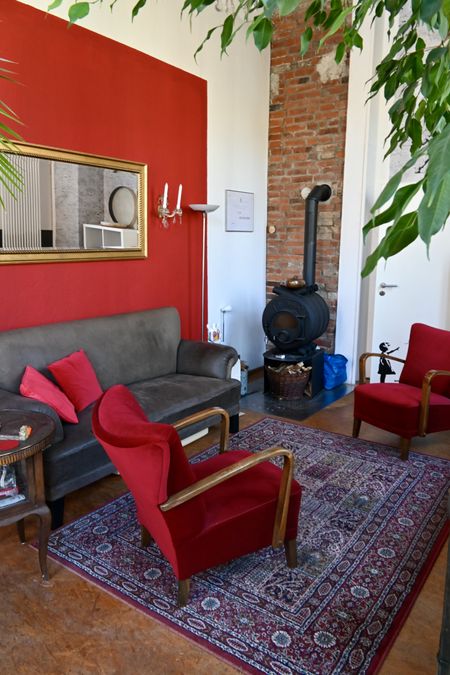 Gemütlicher Raum mit Sofa, Sessel, einem alten Ofen vor eine roten Wand.